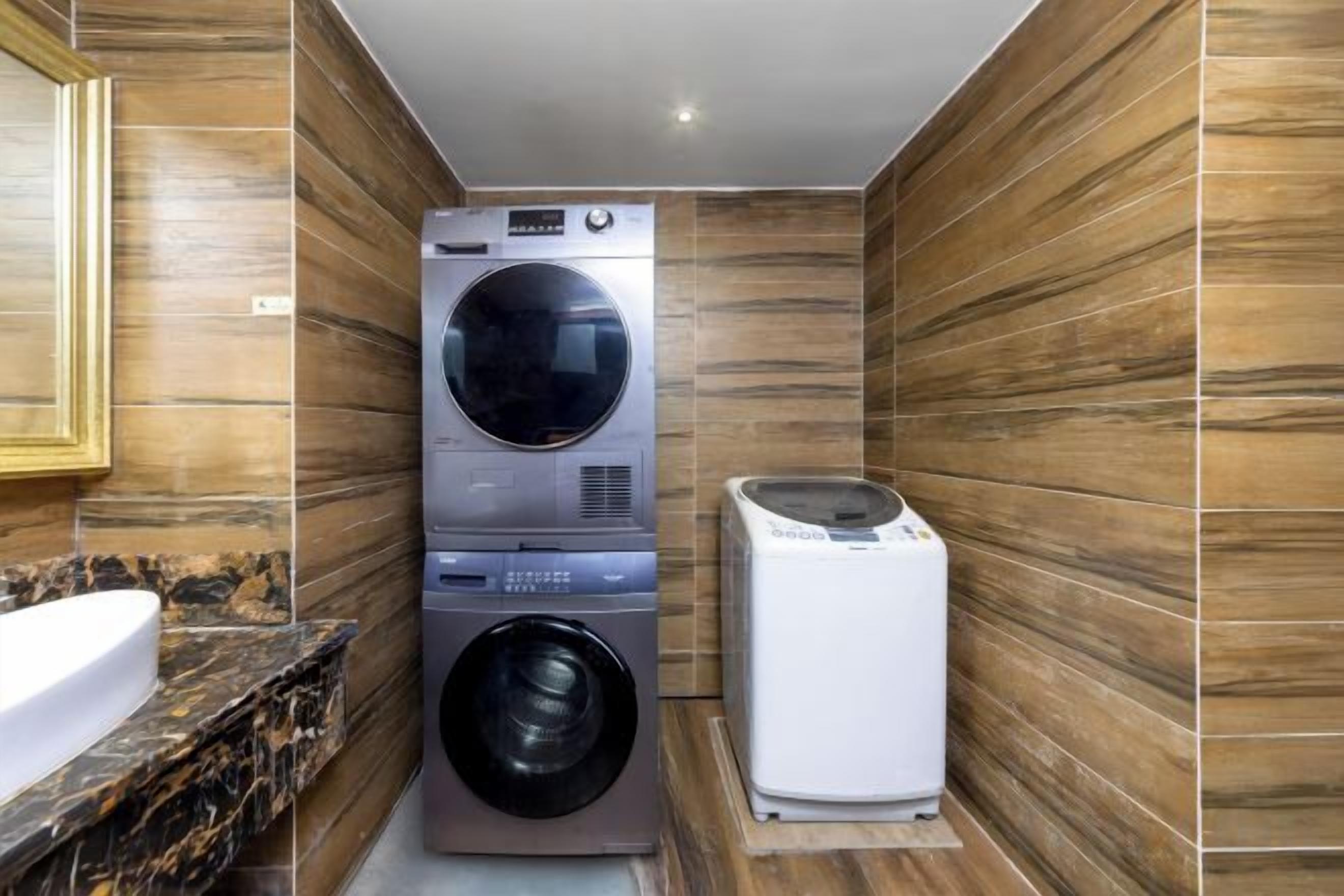 A compact laundry room with stacked appliances, a sink, and wooden walls.