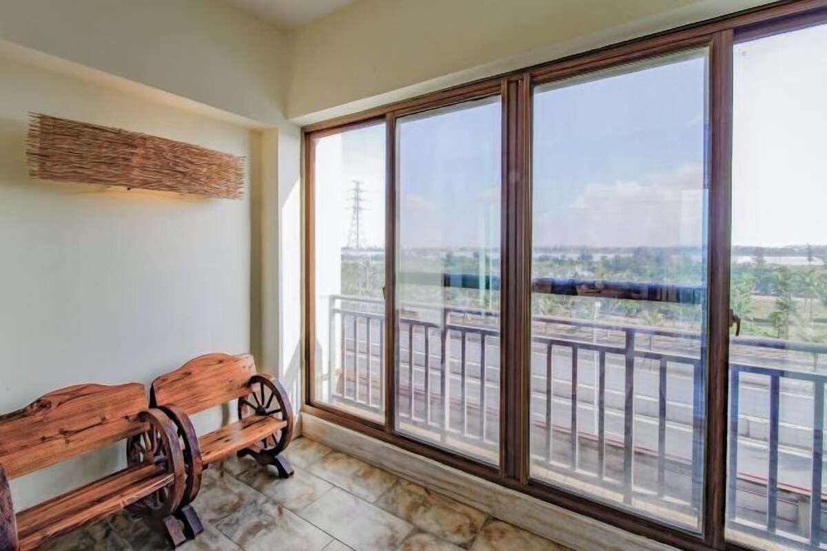 A balcony with a wooden bench, large windows, and a view of a road and buildings.