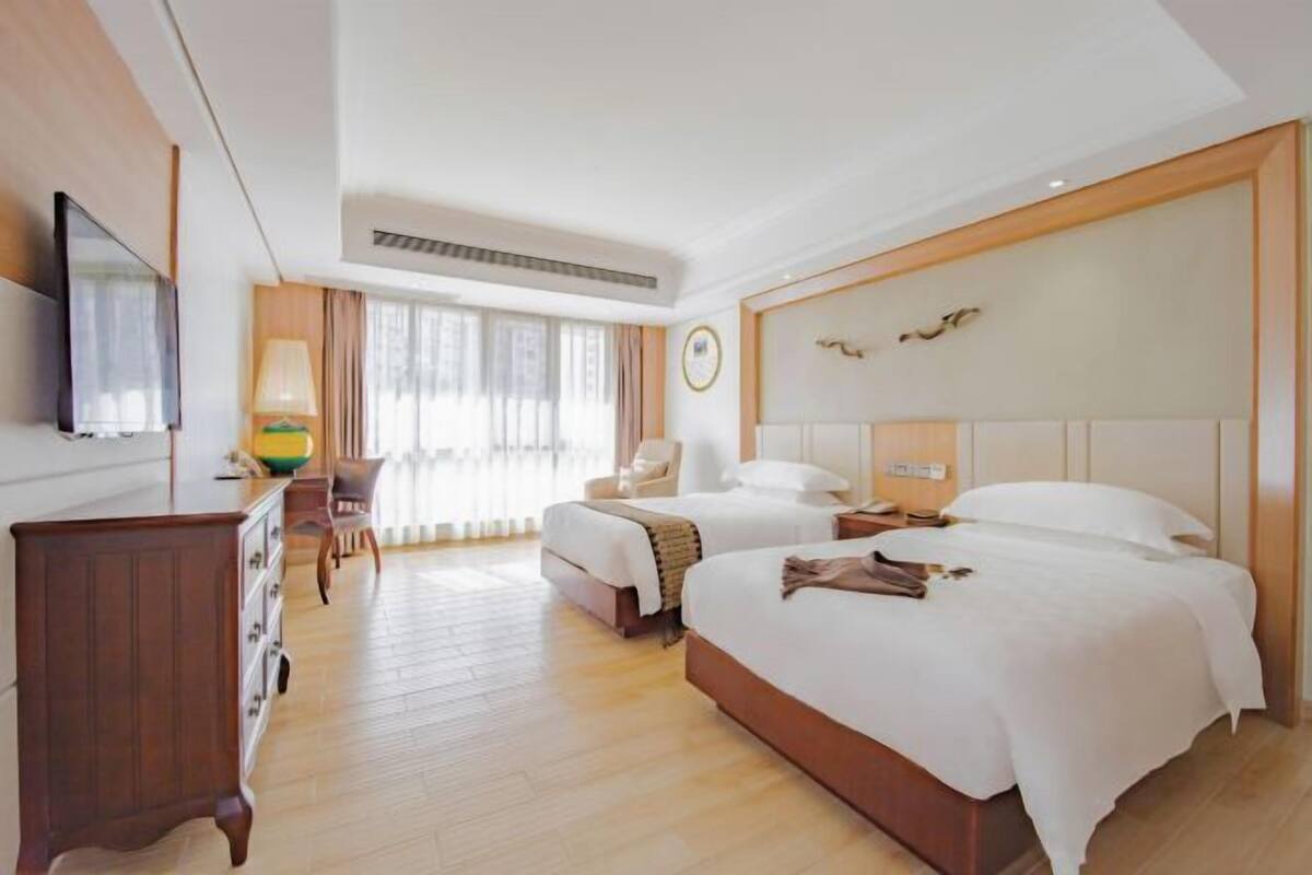 A hotel room with two beds, a TV, a desk with a lamp, and a window with curtains.