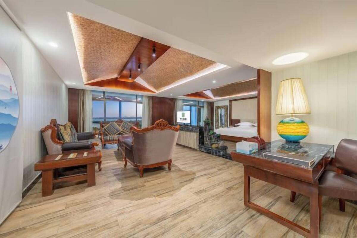 A hotel room with a wooden floor, a large window, a bed, a desk with a lamp, and a globe.