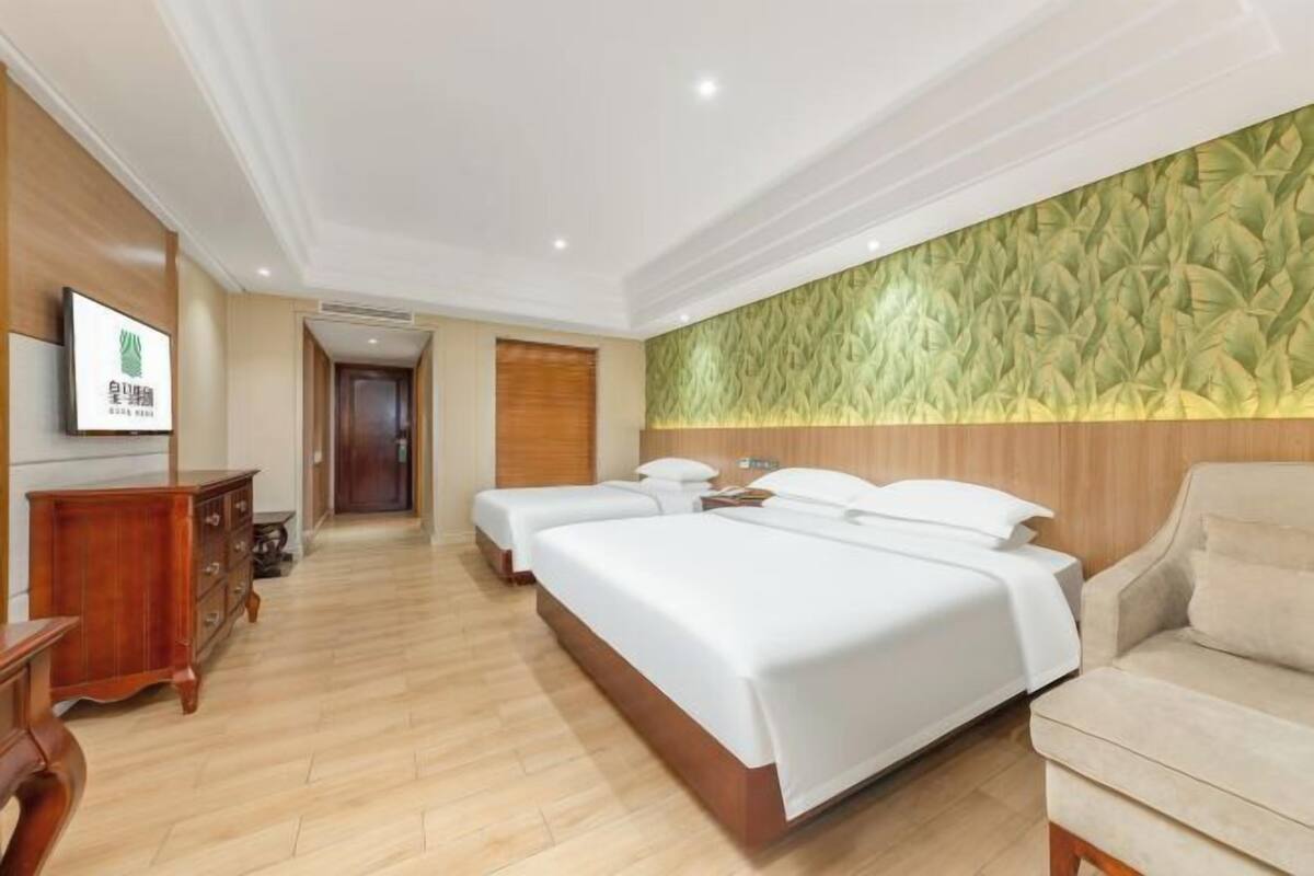 A hotel room with a large bed, two bedside tables, a wooden dresser, and a wall-mounted TV.