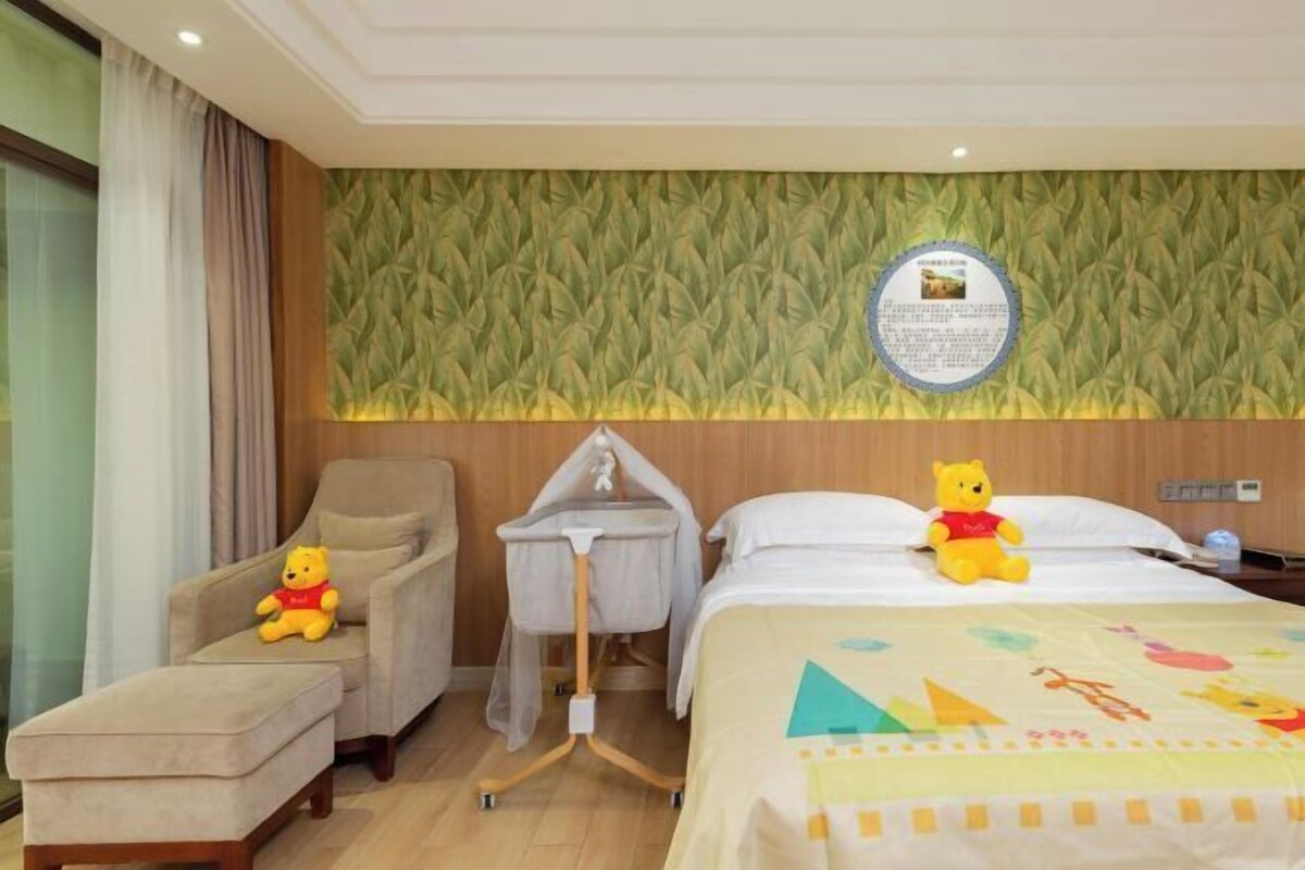 A hotel room with a bed, a chair, a baby stroller, and two Winnie the Pooh toys.