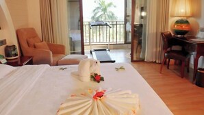 A hotel room with a bed, a chair, a desk, a lamp, and a view of a balcony with a palm tree. - Real Madrid Holiday Island Style Hotel (Haikou Qilou Old Street) (Haikou)