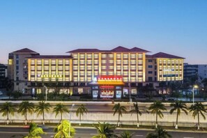 A multi-story hotel with a central entrance, palm trees in the foreground, and a clear sky. - Real Madrid Holiday Island Style Hotel (Haikou Qilou Old Street) (Haikou)