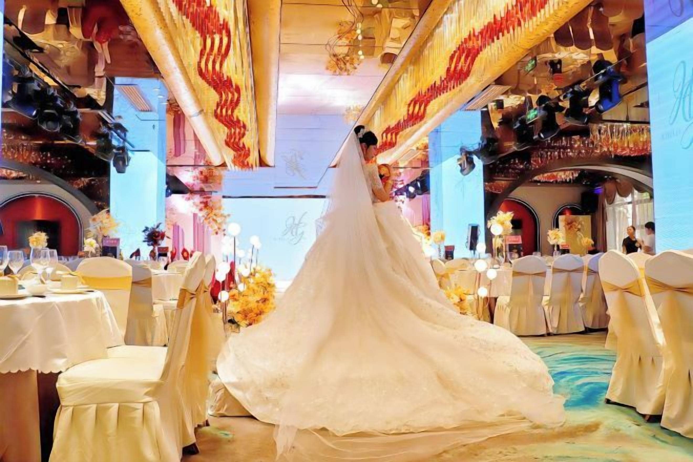 Una cerimonia nuziale in una sala da banchetti con tavoli apparecchiati per gli invitati, decorazioni floreali e una sposa con un abito bianco.