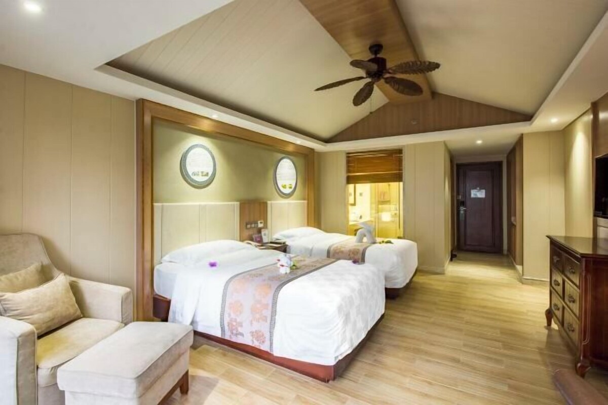 A hotel room with a large bed, a sofa, a desk, and a ceiling fan.