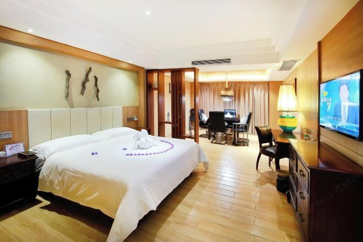 A hotel room with a large bed, a desk with a computer, a television, and a wooden floor.