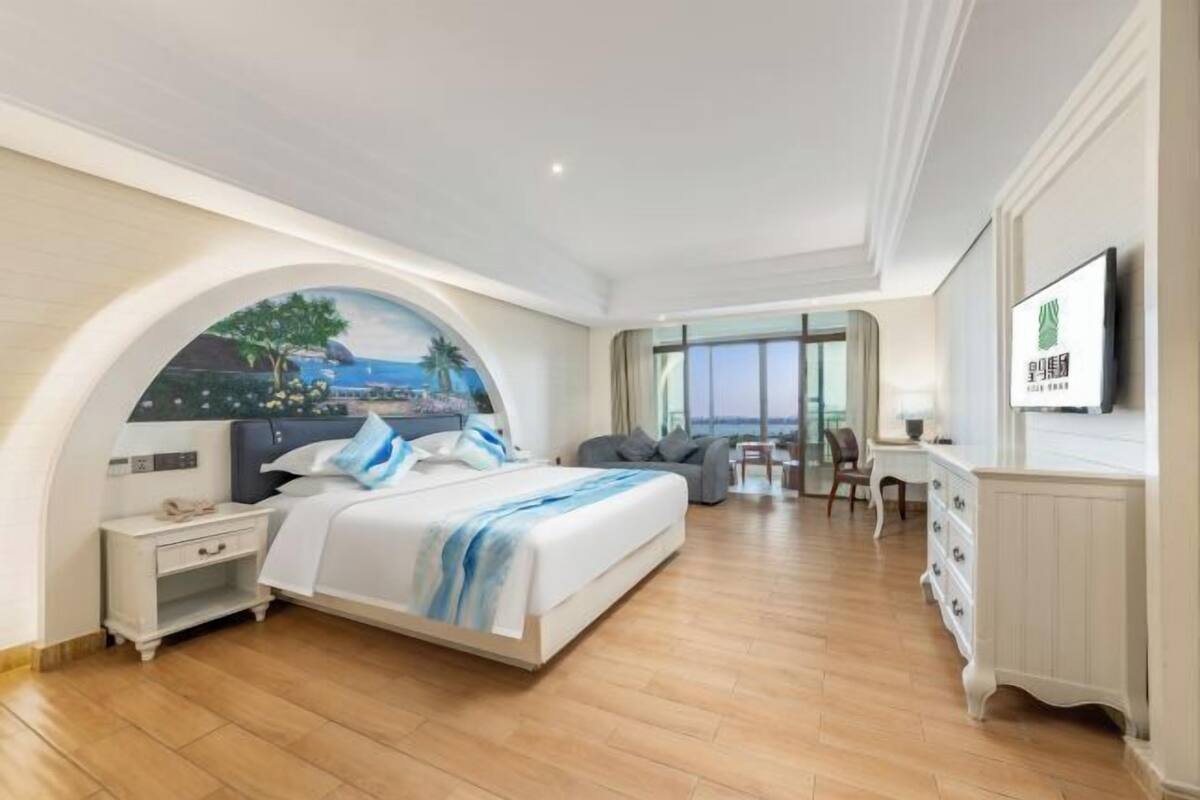 A hotel room with a bed, a desk, a chair, a TV, and a large window with a view.