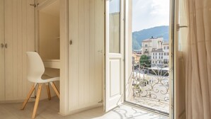 A room with a white chair, a wooden desk, and a large window with a view of buildings and mountains. - Linda Apartment 2 in Como (Como)