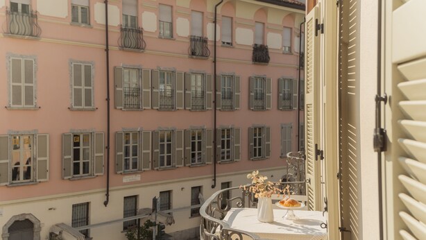 A balcony with a table set for dining, overlooking a row of buildings with uniform architecture. - Linda Apartment 2 in Como (Como)