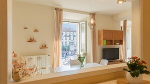 A modern living room with a large window, a television, and a dining area with a table and chairs. - Linda Apartment 2 in Como (Como)