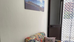 A colorful sofa with a patterned cover, a potted plant, and a framed picture on the wall. - Garden villa – your relaxed base to explore West Sicily (Custonaci)