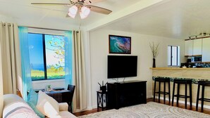 Una sala de estar con sofá, televisor, mesa de comedor y zona de cocina con microondas.