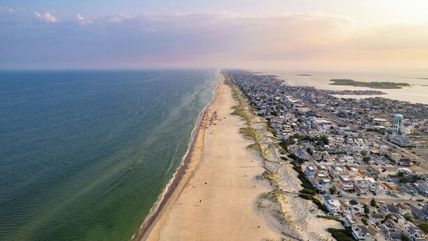 Vista aérea de un pueblo costero con una playa larga y arenosa, una zona residencial densa y una torre de agua.