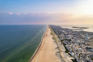 An aerial view of a coastal town with a long sandy beach, a dense residential area, and a water tower.