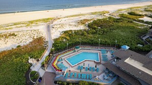 Vista aérea de un complejo turístico con una gran piscina, acceso a la playa y abundante vegetación.