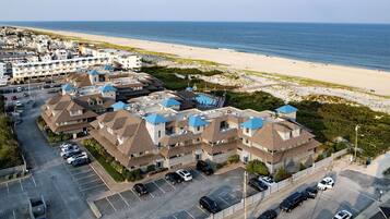 A coastal hotel with multiple buildings, a parking lot, and a beach view.