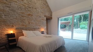 Une chambre avec un mur en pierre, un cadre de lit en bois et une grande porte-fenêtre coulissante donnant sur un espace extérieur.