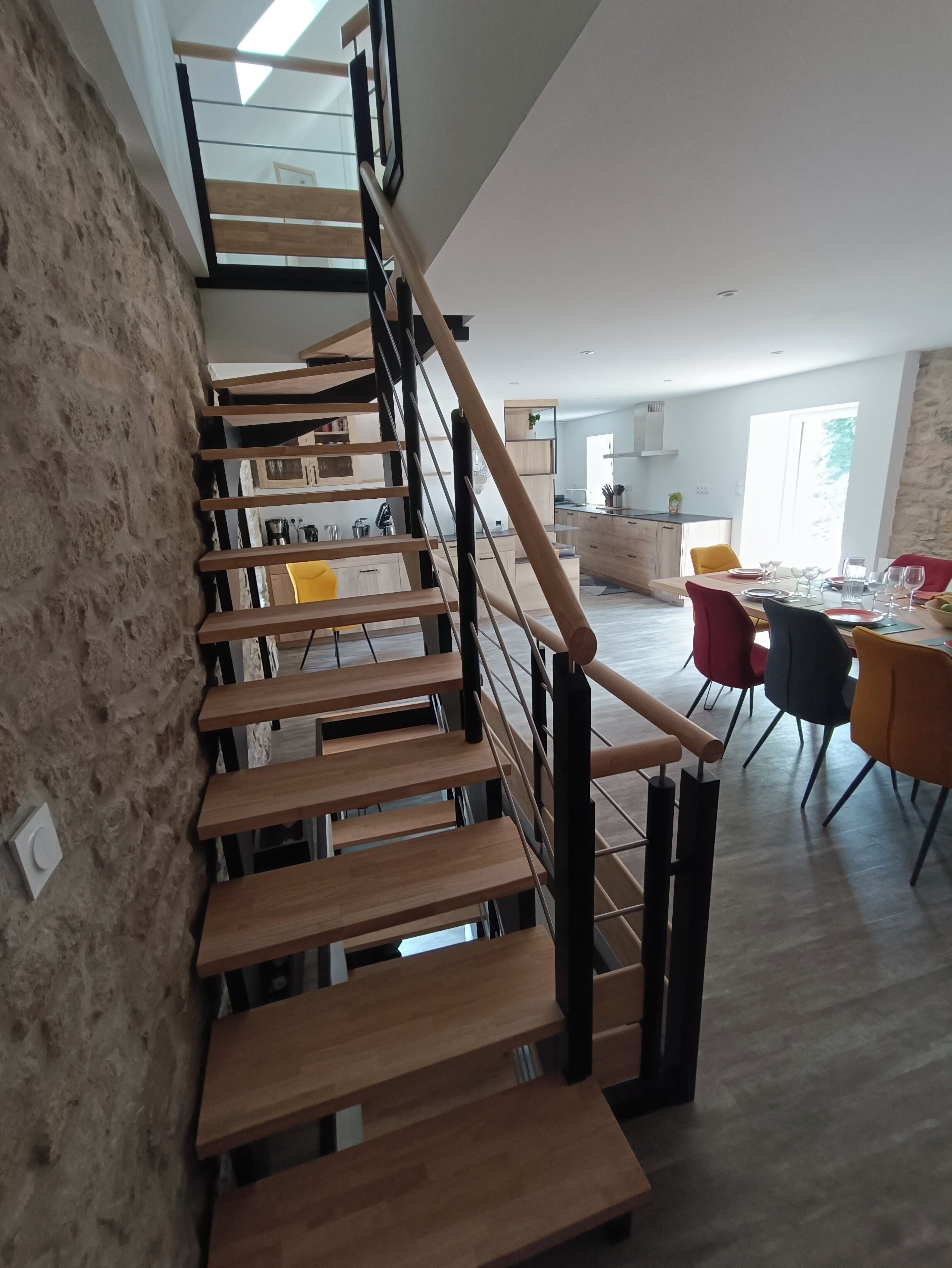 Un intérieur moderne avec un escalier en bois, un coin repas avec des chaises et une cuisine en arrière-plan.