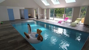 Une piscine intérieure avec un jouet gonflable en forme de dauphin, de grandes fenêtres et une vue sur l’extérieur.