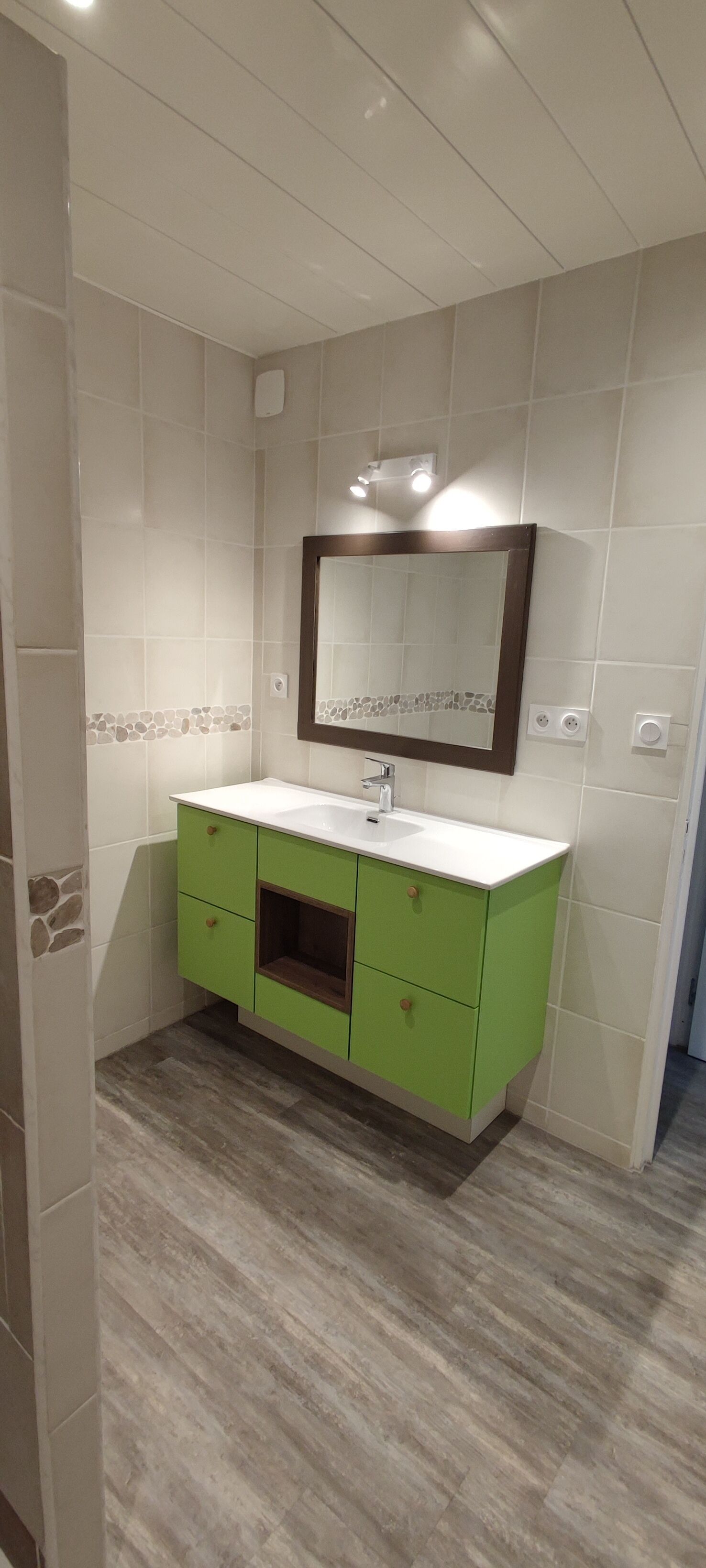 A bathroom with a green vanity, white tiles, a mirror, and a light fixture.