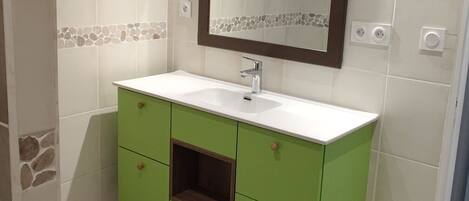A bathroom with a green vanity, white tiles, a mirror, and a light fixture.