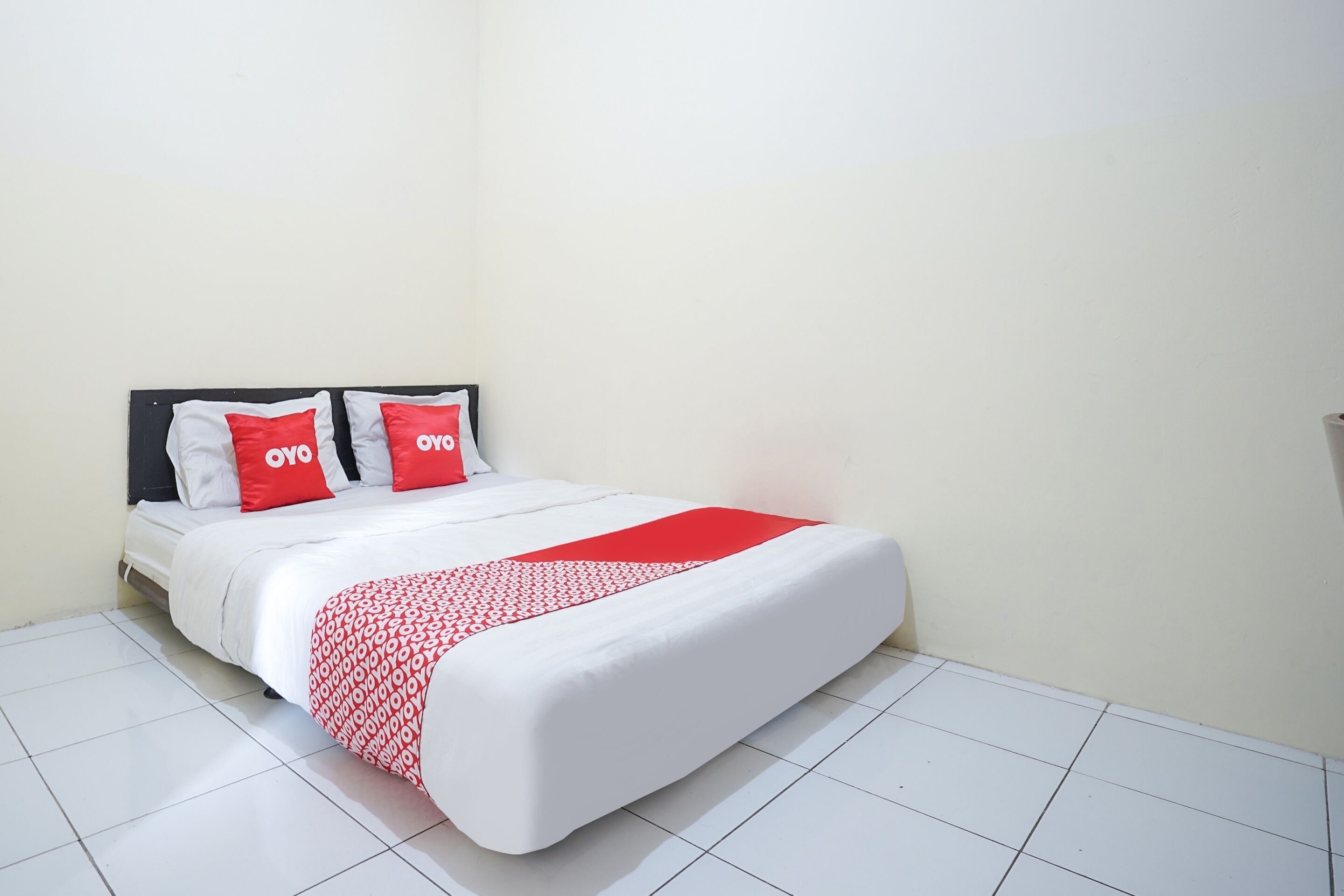 A neatly made bed with a white and red bedspread, two red pillows with "OYO" branding, and a black headboard.