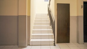 A staircase with white steps and a metal railing, leading to a dark door. - Hotel O Seturan Near Hartono Mall Yogyakarta Formerly Maleo Kostel (Depok)