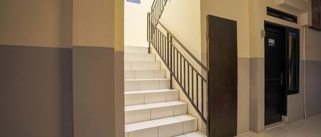 A staircase with white tiles and black railings, leading to a door with a sign above it.