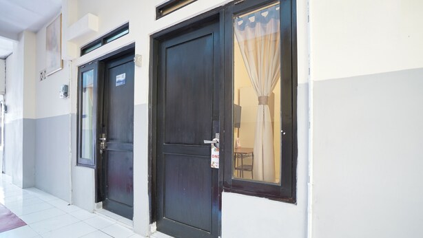 A hotel entrance with two dark wooden doors, a tiled floor, and a window with a curtain. - Hotel O Seturan Near Hartono Mall Yogyakarta Formerly Maleo Kostel (Depok)