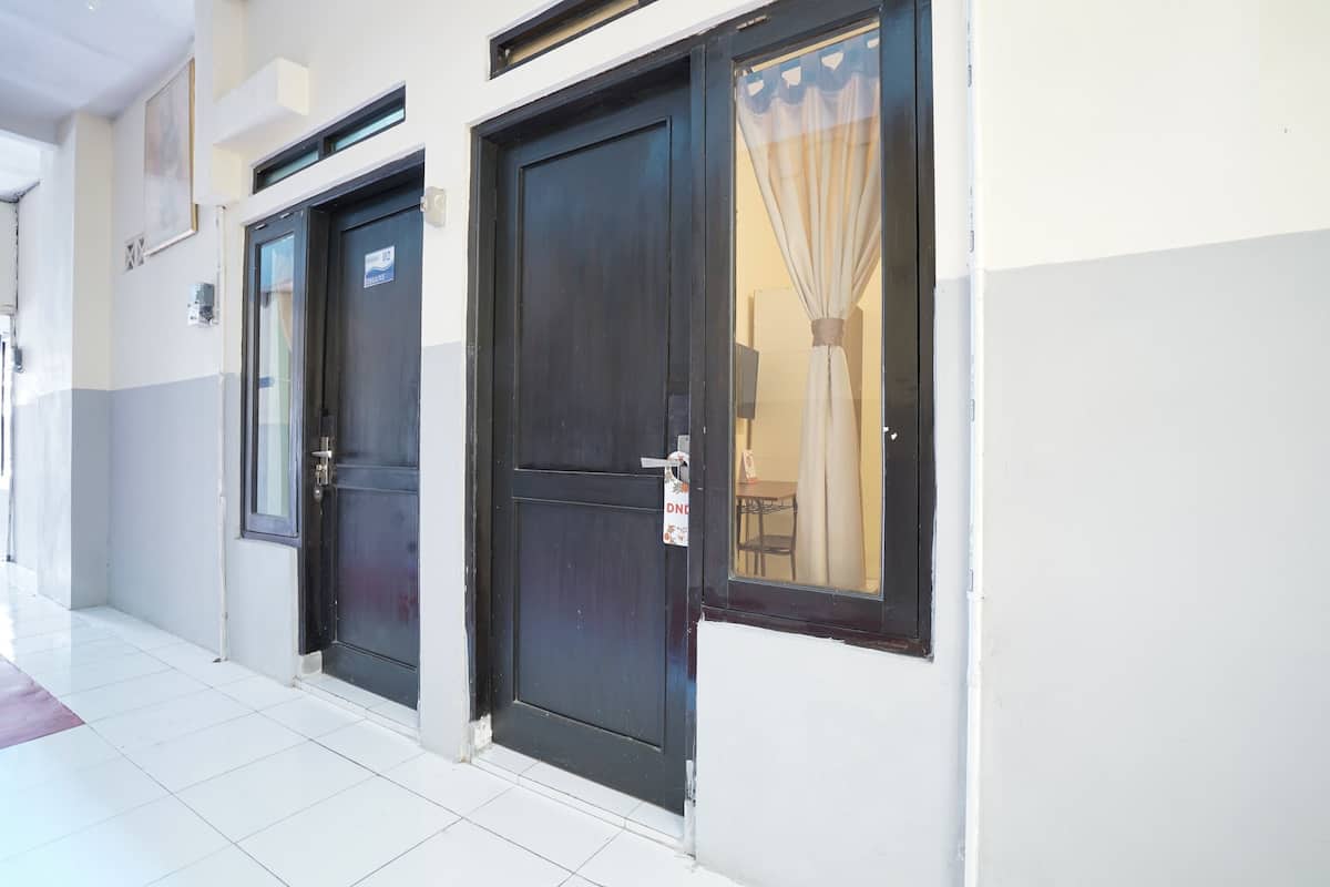 A hotel entrance with two dark wooden doors, a tiled floor, and a window with a curtain.