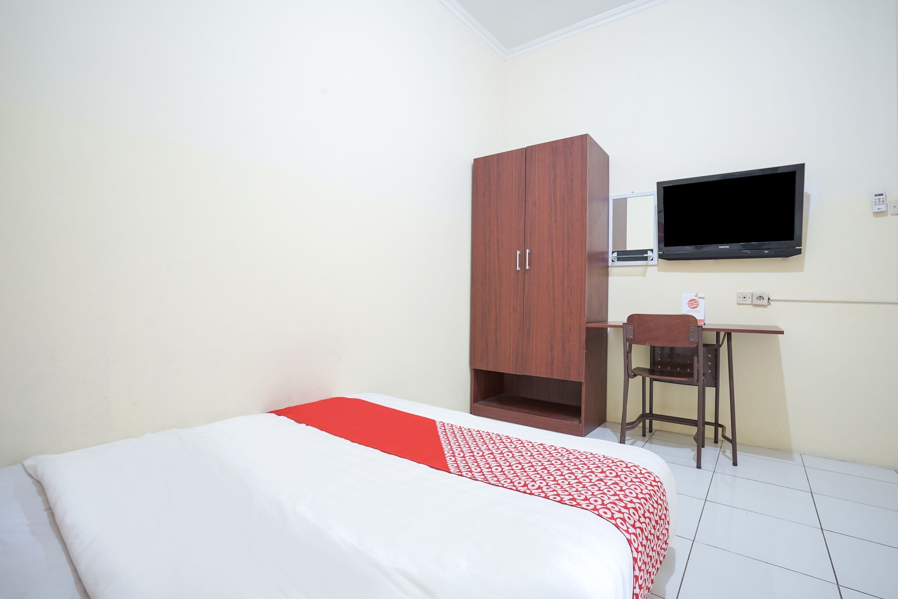 Une chambre d’hôtel comprenant un lit, une armoire en bois, un bureau avec une chaise et un téléviseur fixé au mur.