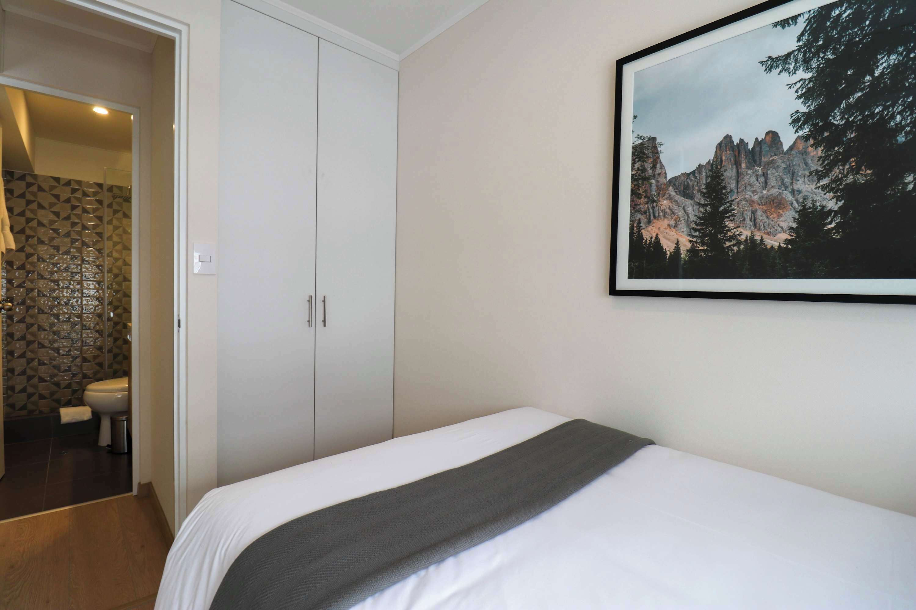 A bedroom with a bed, a wardrobe, and a framed picture of a mountain landscape on the wall.