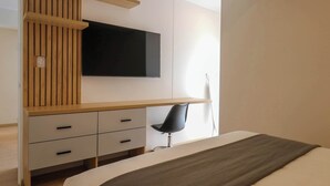 A modern bedroom with a bed, a desk with a chair, a TV mounted on the wall, and a wooden panel design on the wall. - w* | Divine 2BR with Majestic Deco in Barranco (Barranco)