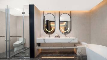 A modern bathroom with a glass shower enclosure, a white toilet, a marble-topped sink with dual mirrors, and a freestanding bathtub.