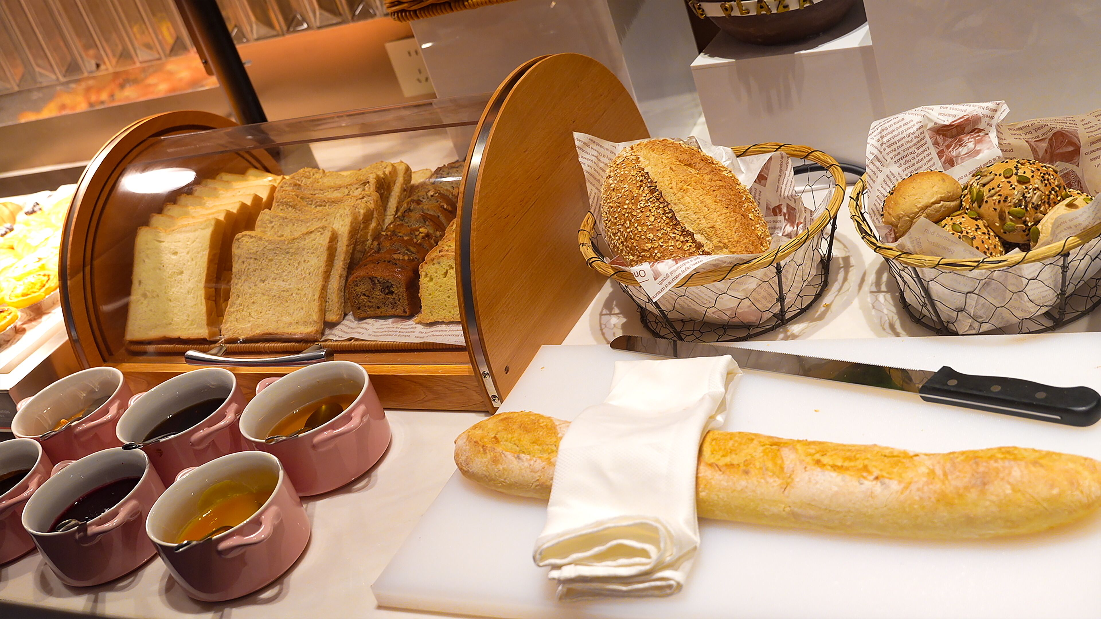 A breakfast buffet with bread, pastries, and coffee cups.