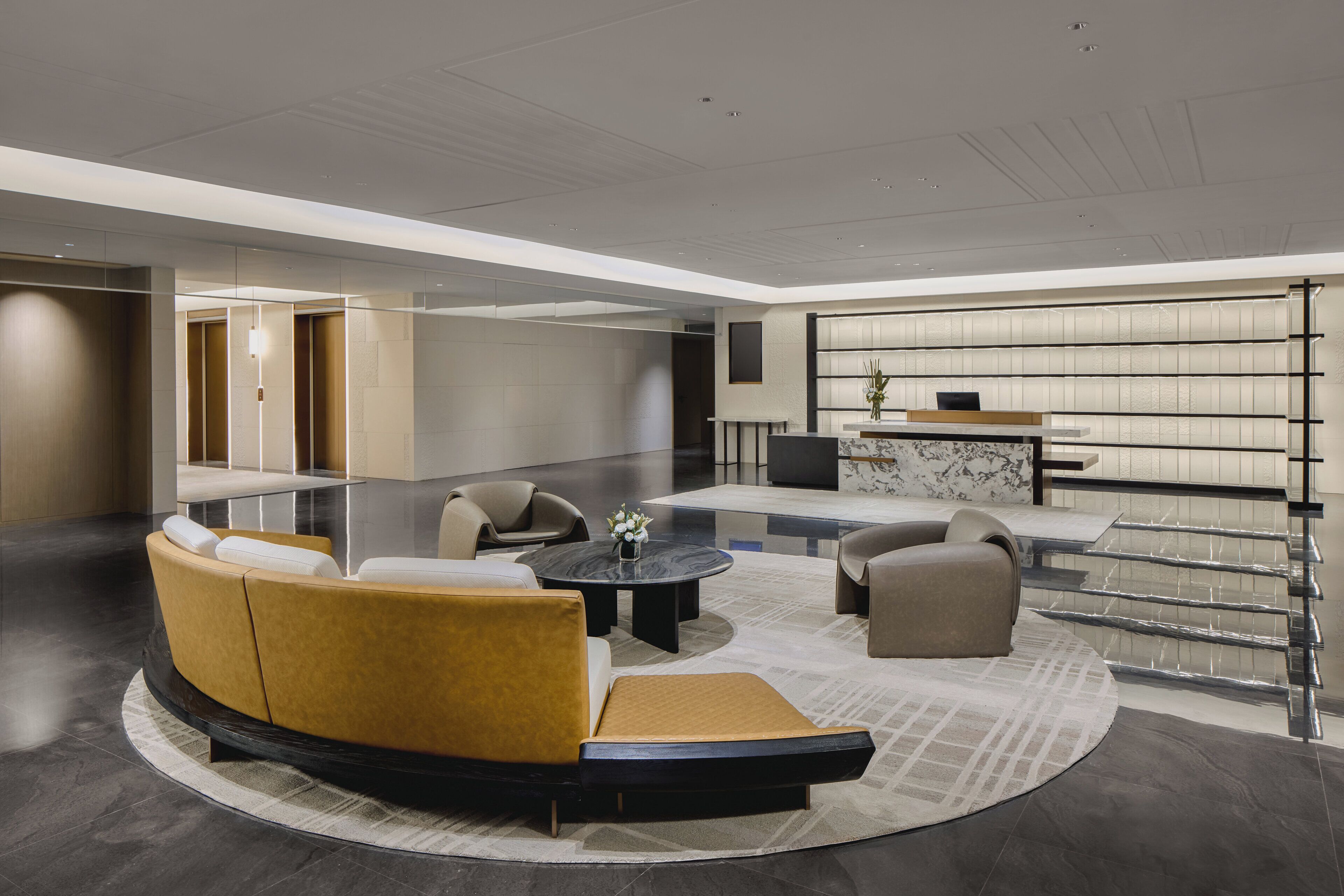 A modern lobby with a curved sofa, a round coffee table, and a seating area with a marble table and chairs.