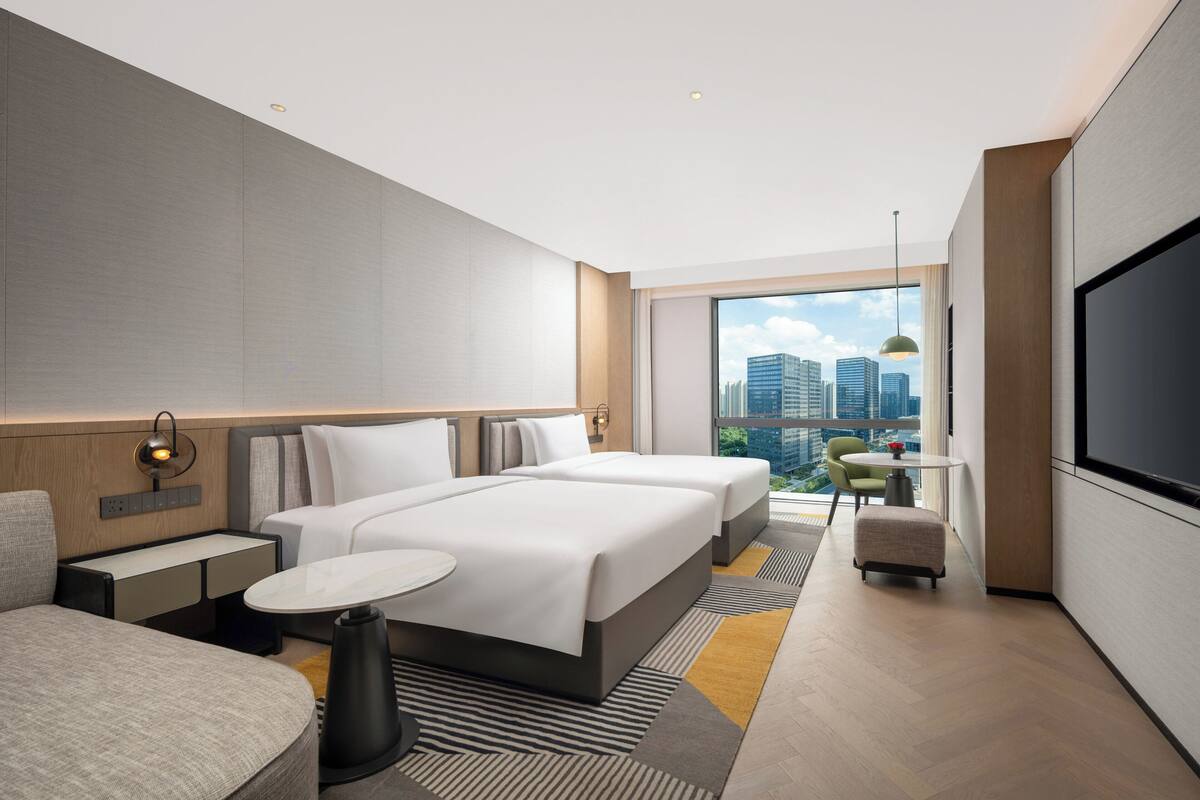 A modern hotel room with a large bed, a desk, a chair, and a TV.