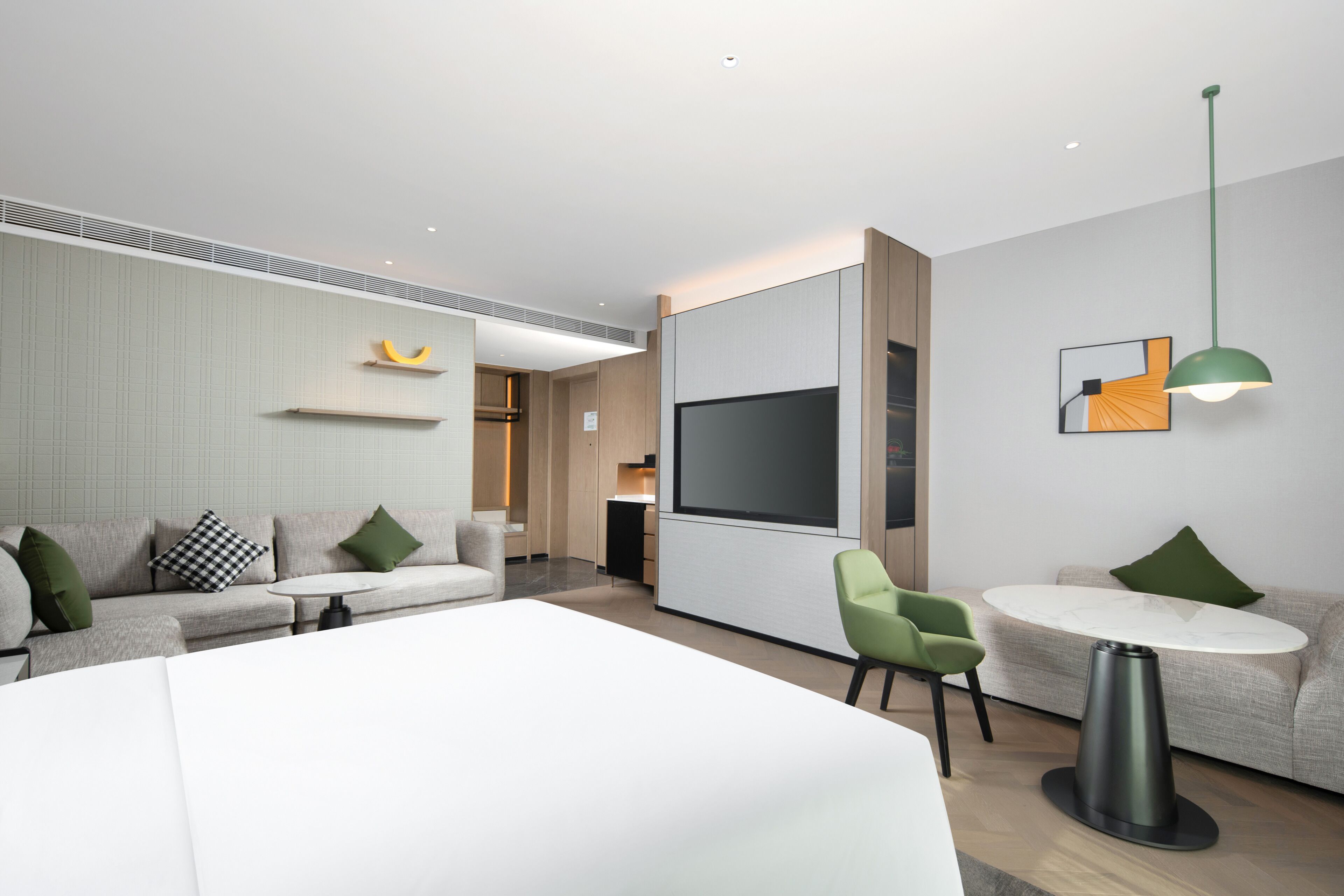 Una moderna camera d'albergo con un ampio letto, una zona salotto con divano e poltrone, una TV e un tavolo da pranzo.
