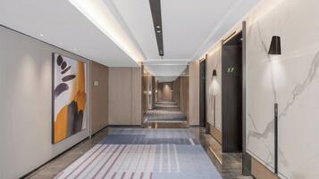 A modern hotel corridor with a long hallway, elevators, and a patterned carpet.