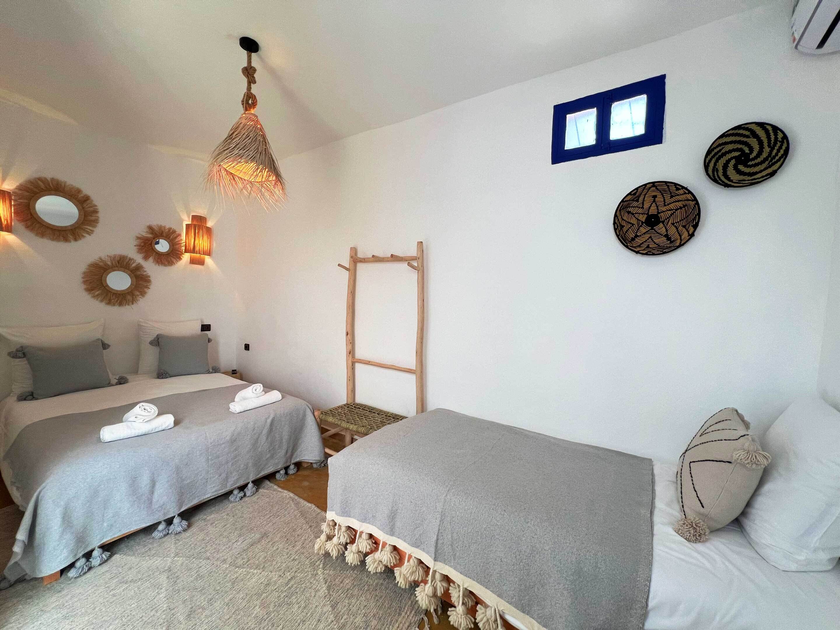 A hotel room with two beds, a hanging light fixture, wall-mounted mirrors, and decorative wall art.