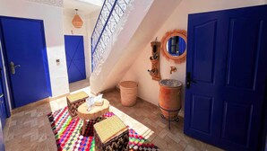 A spacious hallway with a high ceiling, a blue staircase, and a colorful rug.