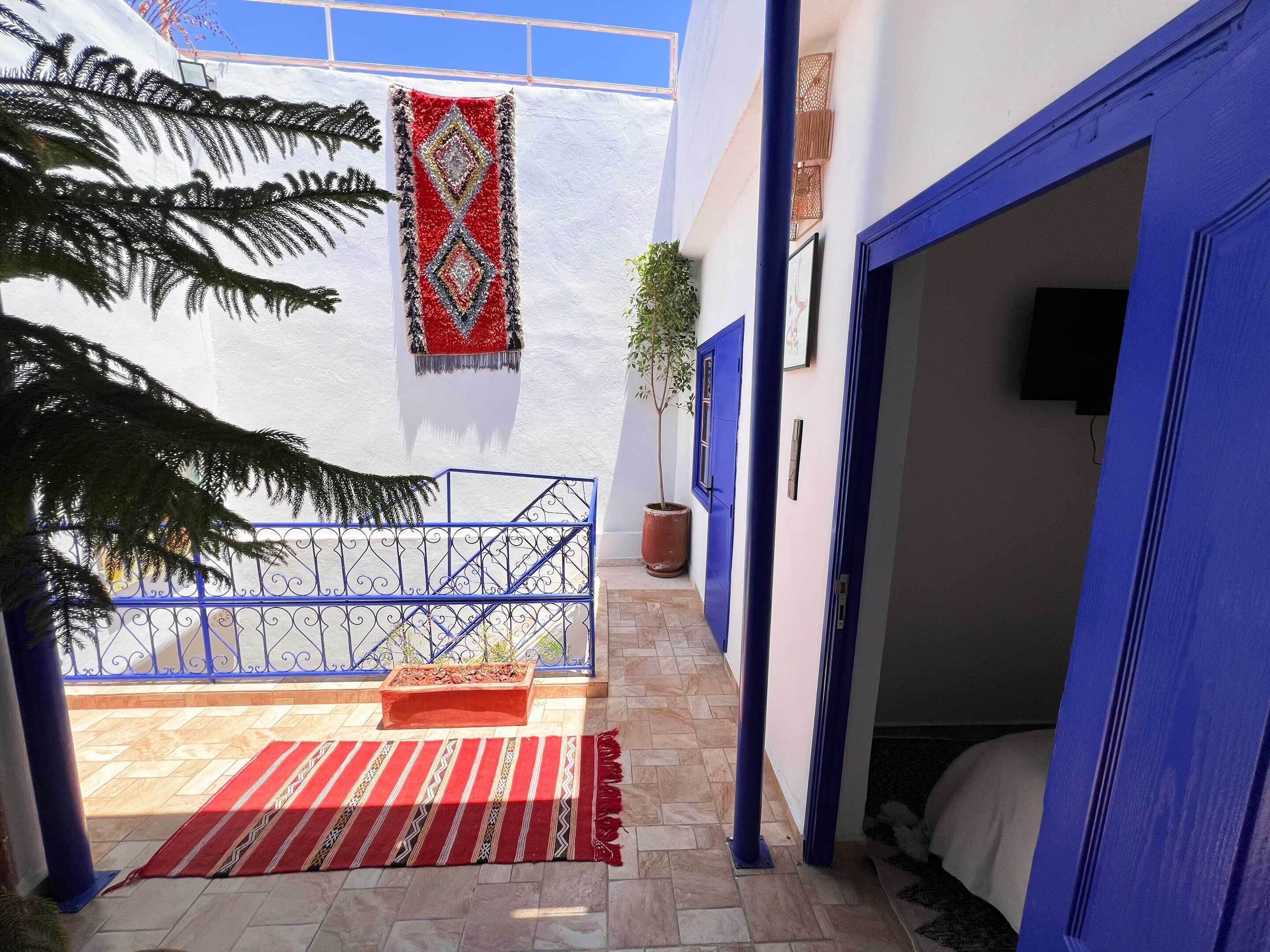 A courtyard with a blue gate, a red and white patterned rug, and a potted plant.