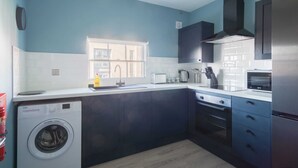 A modern kitchen with dark cabinets, a built-in washing machine, and a window providing natural light. - Charming 1 Bedroom Apartment in Central Liverpool (Liverpool)