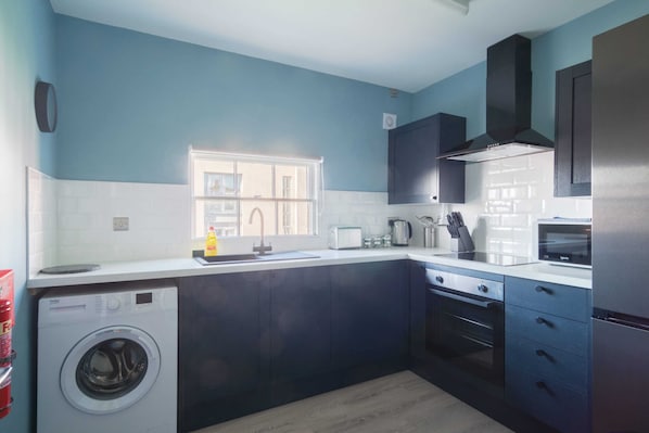 A modern kitchen with dark cabinets, a built-in washing machine, and a window providing natural light.