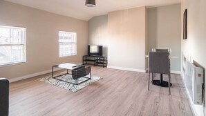 A spacious living room with a flat-screen TV, a coffee table, and a dining area with a chair and table. - Charming 1 Bedroom Apartment in Central Liverpool (Liverpool)