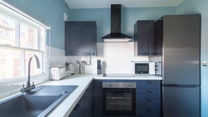 A modern kitchen with a stainless steel sink, a built-in oven, a microwave, and dark cabinetry. - Charming 1 Bedroom Apartment in Central Liverpool (Liverpool)