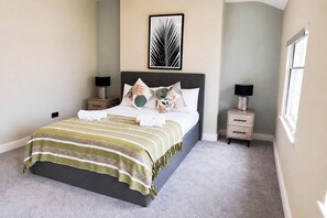 A neatly made bed with a striped bedspread, two bedside tables with lamps, a wall art piece above the bed, and a window on the right.