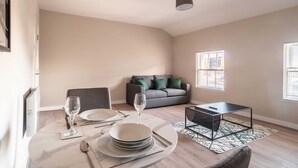A dining area with a round table set for two, a grey sofa, and a black coffee table. - Charming 1 Bedroom Apartment in Central Liverpool (Liverpool)