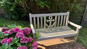 A wooden bench with a simple backrest and armrests, positioned on a brick pathway. - Experience Frisian coziness in Haus Siril and the Kombüse apartment on Wangerooge (Wangerooge)